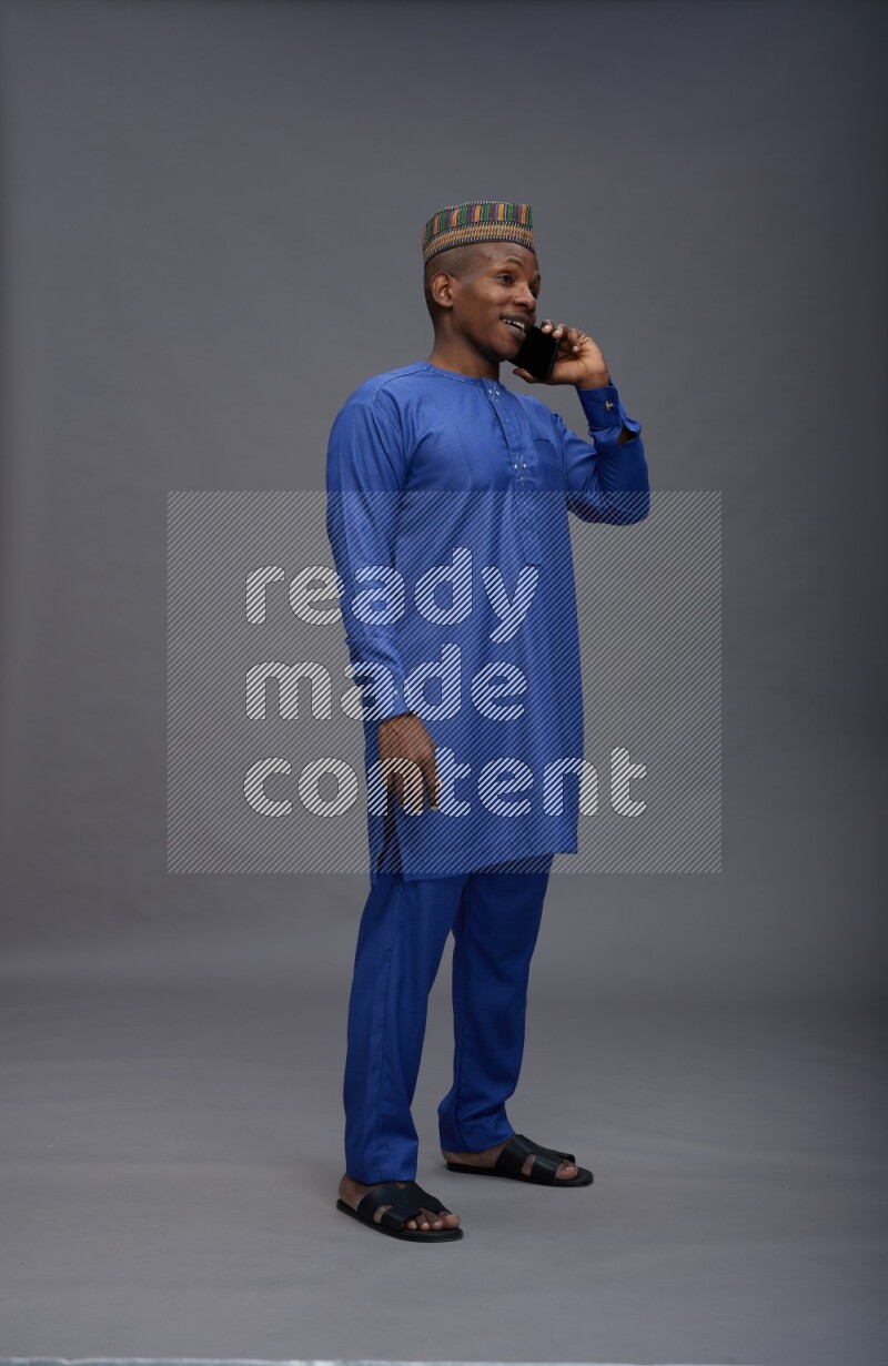 Man wearing Nigerian outfit standing talking on phone on gray background