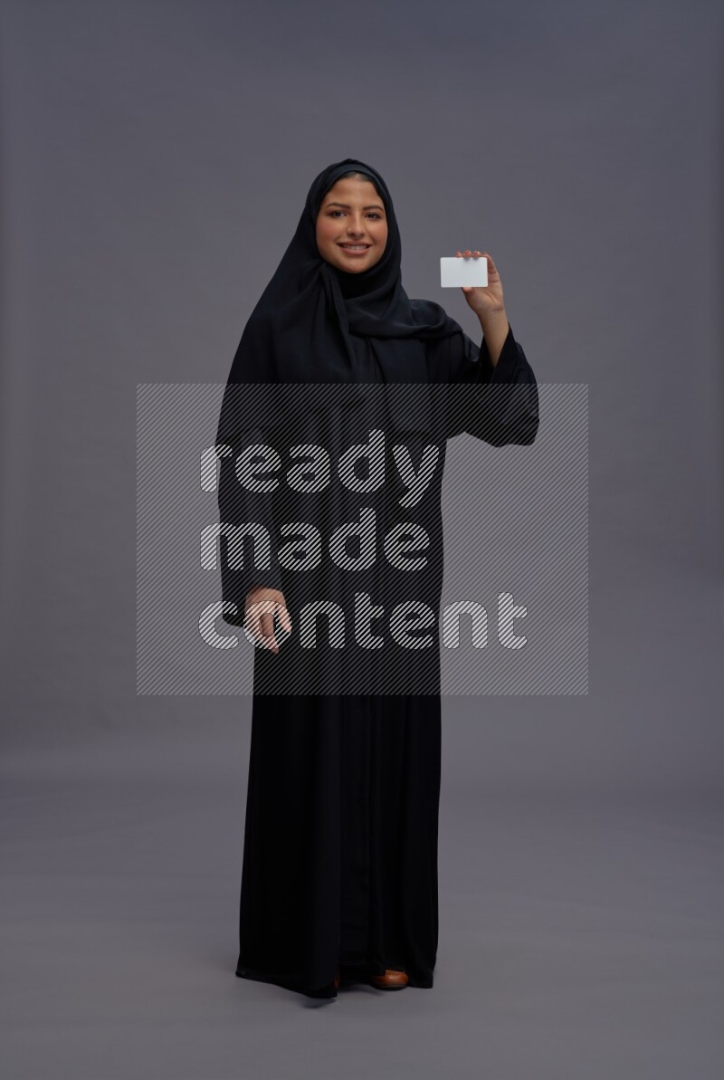 Saudi woman wearing Abaya standing holding ATM card on gray background