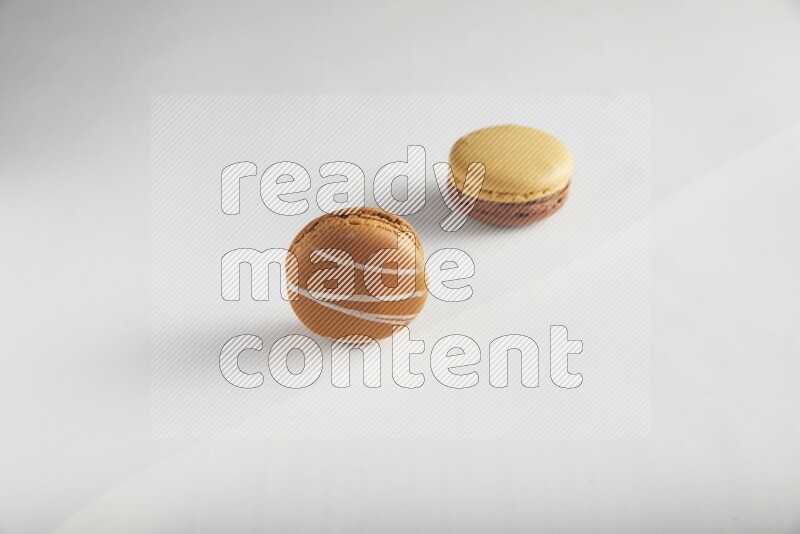 45º Shot of of two assorted Brown Irish Cream, and Yellow, and Brown Chai Latte macarons on white background