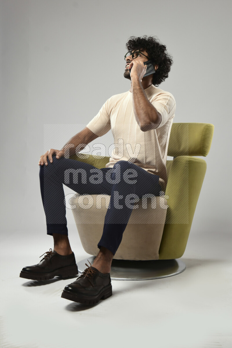 A man wearing casual sitting on a chair talking on the phone on white background