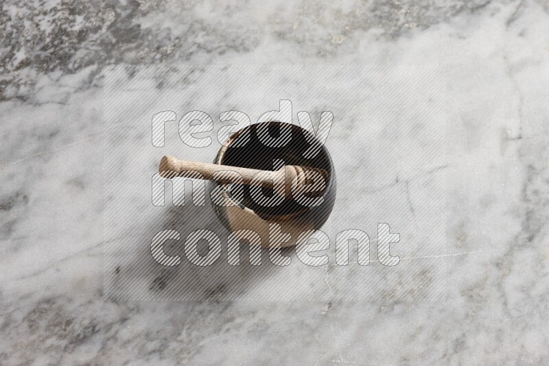 Multicolored pottery bowl with wooden honey dipper in it on grey marble background