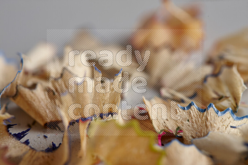 A close-up showing a small pile of pencil shavings with varied color edges on grey background
