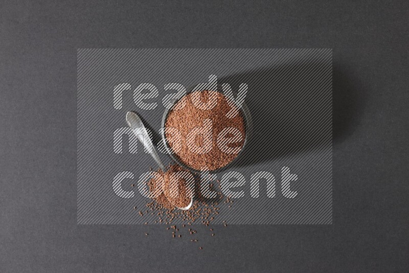 A black pottery bowl full of garden cress seeds and metal spoon full of the seeds on a black flooring