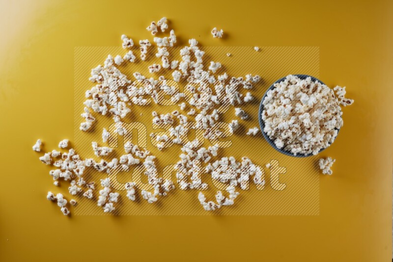 A blue pottery bowl full of popcorn with popcorn beside it on a yellow background in different angles