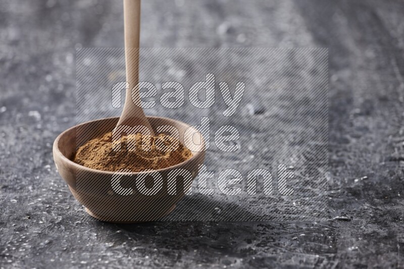 Wooden bowl full of cinnamon powder with a wooden spoon on a textured black background in different angles