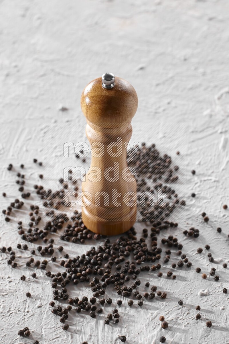A wooden grinder with black pepper beads on a textured white flooring