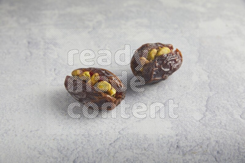 two pistachio stuffed madjoul date on a light grey background