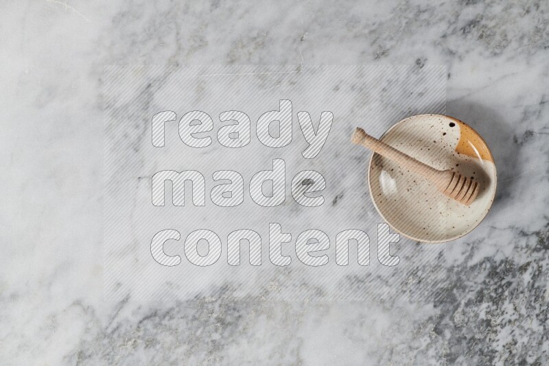 طبق فخاري متعدد الألوان مع ملعقة عسل خشبية بداخله على خلفية من الرخام الرمادي