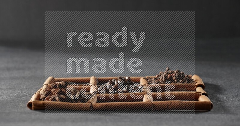 9 squares of cinnamon sticks full of coffee beans in the middle surrounded by nutmeg, dried mint, cloves, dried basil, dried ginger, cinnamon, star anise and cardamom on black flooring