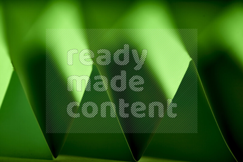 A close-up abstract image showing sharp geometric paper folds in green gradients