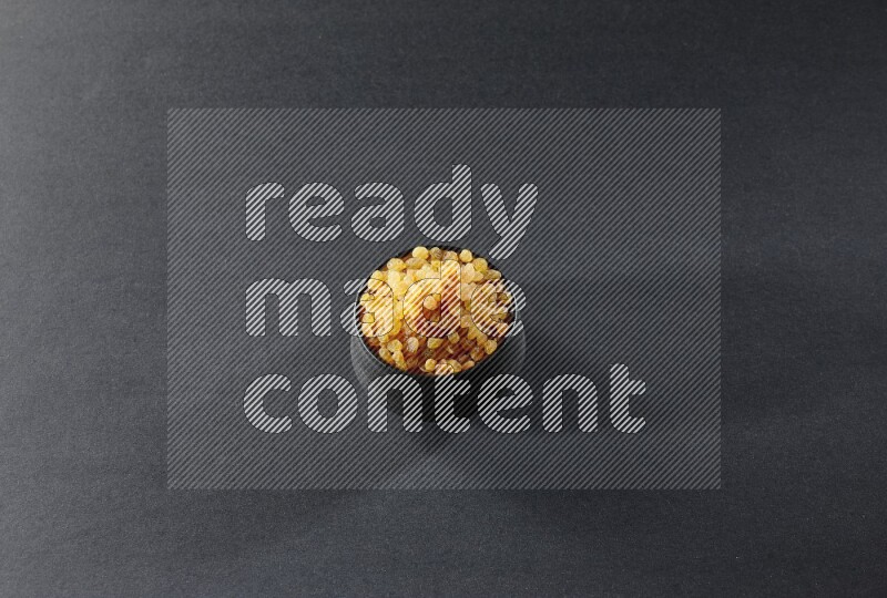 وعاء فخاري أسود ممتلئ بالزبيب الأصفر على خلفية سوداء