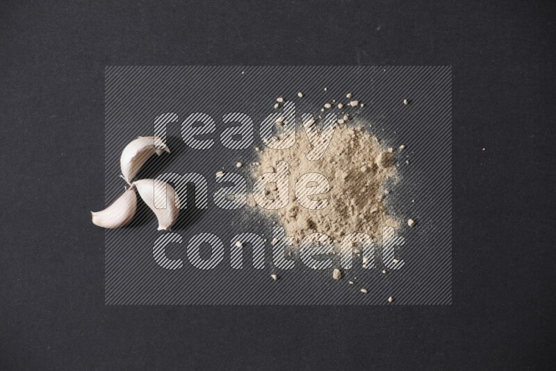 كومة صغيرة من بودرة الثوم مع بعض فصوص الثوم ورأس ثوم كاملة على خلفية سوداء