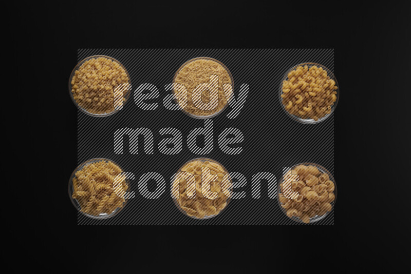 Different pasta types in 6 glass bowls on black background