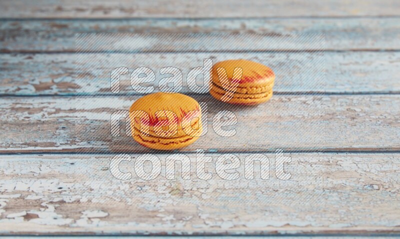 45º Shot of two orange Exotic macarons on light blue wooden background