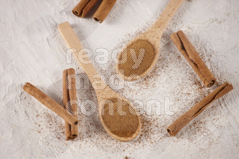 Two wooden spoons full of cinnamon powder with cinnamon sticks on white background