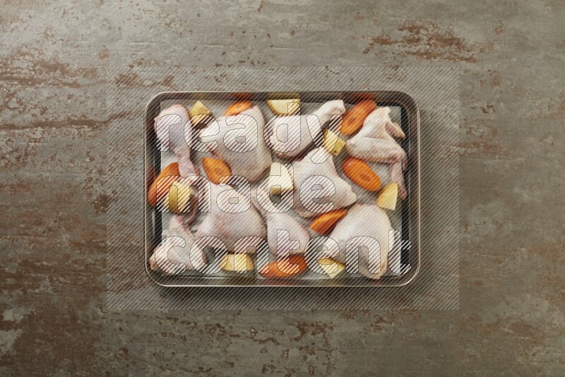 Mixed fresh chicken pieces in an oven tray on a textured rustic background