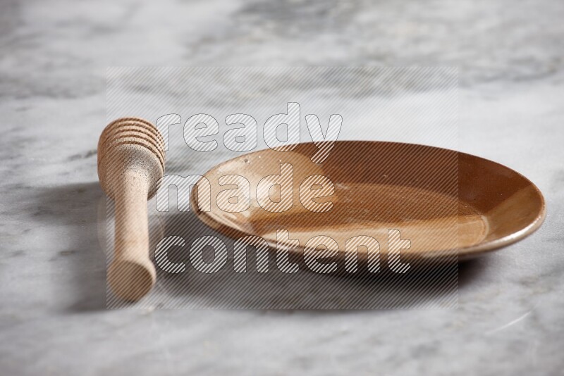 Multicolored pottery plate with wooden honey dipper on the side on grey marble background
