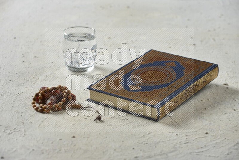 Quran with dates, prayer beads and different drinks all placed on textured white background