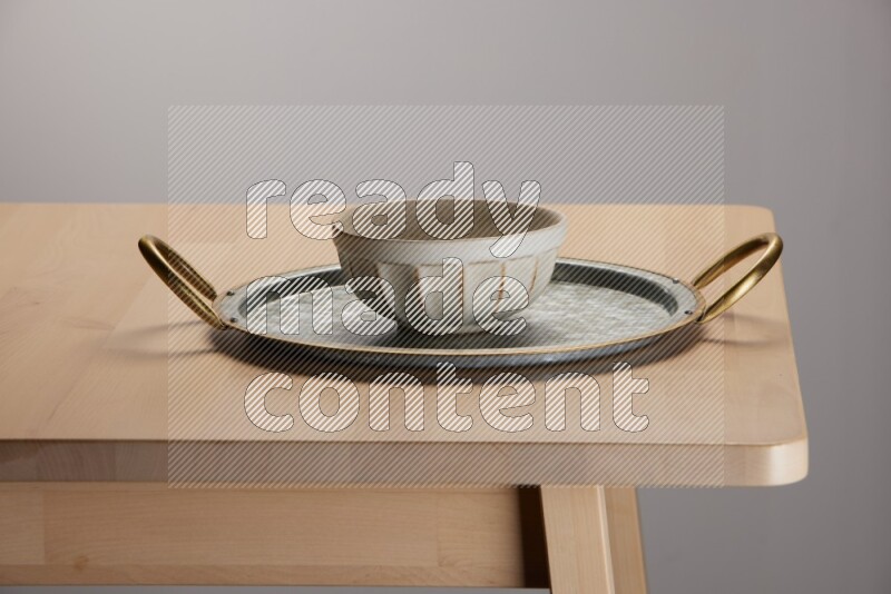 off white bowl placed on a rounded stainless steel tray with golden handels on the edge of wooden table