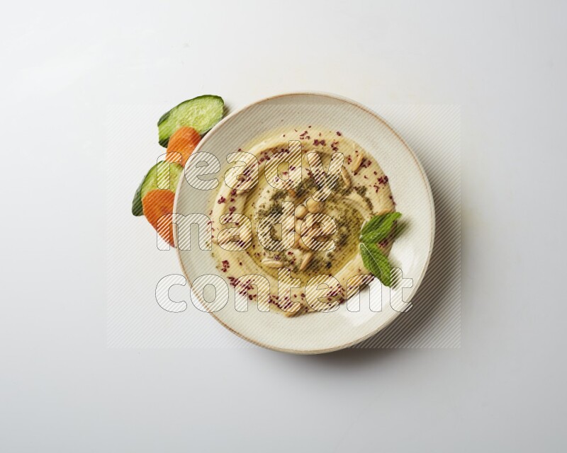 Hummus in a pottry plate garnished with zaatr & sumak on a white background