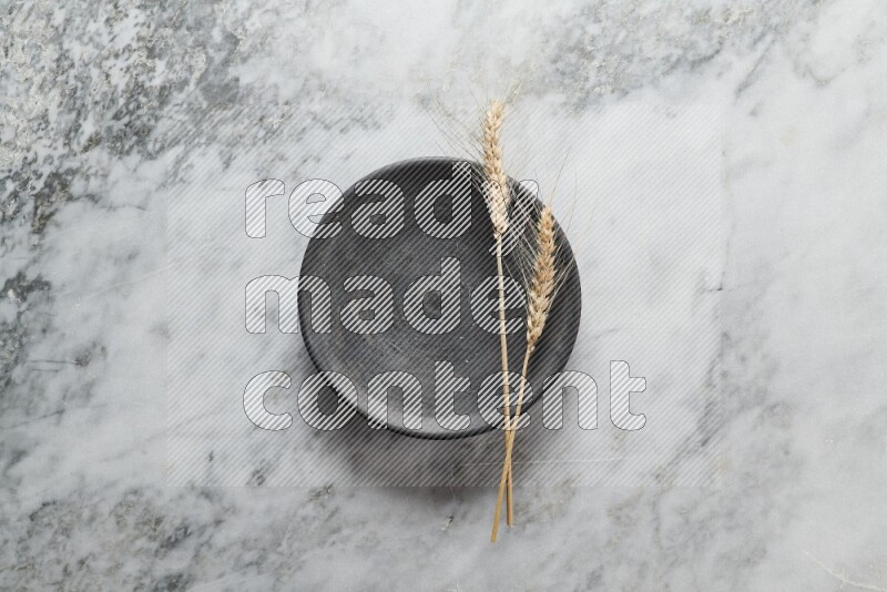 Wheat stalks on black pottery plate on grey marble background