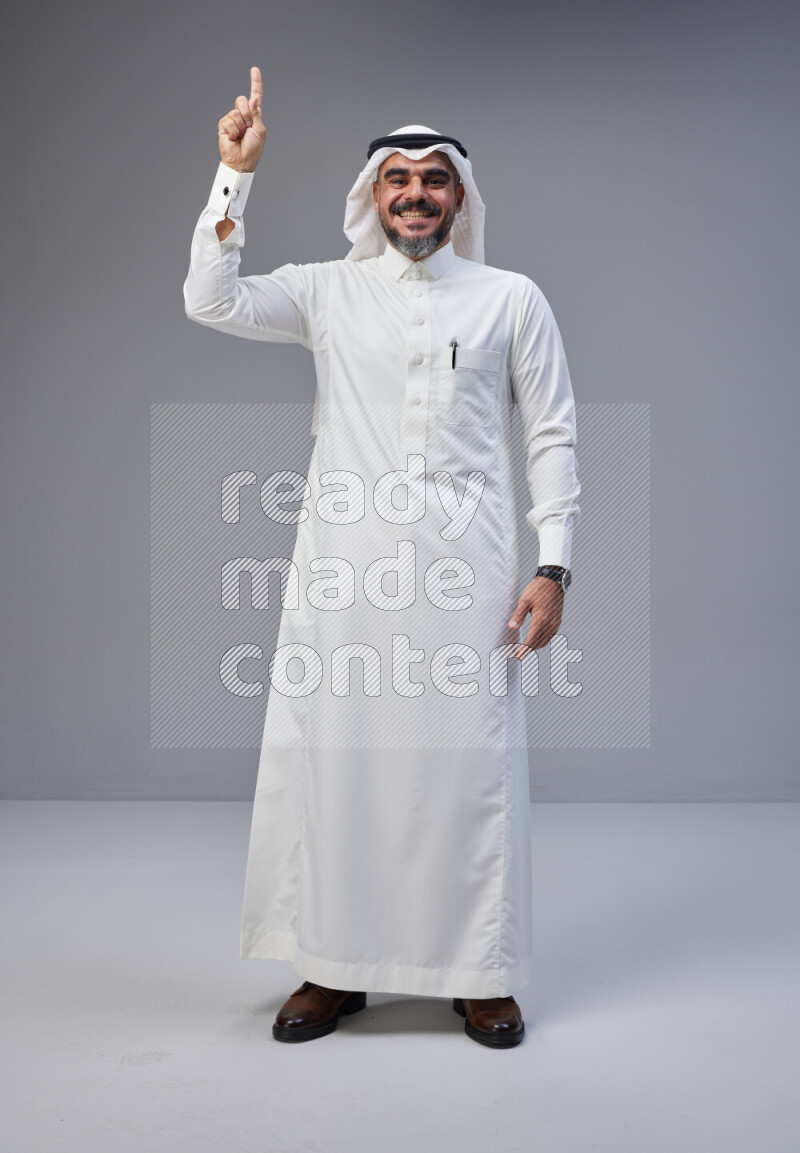 Saudi man Wearing Thob and white Shomag standing interacting with the camera on Gray background