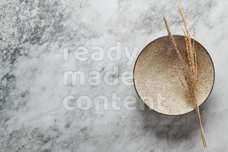 Wheat stalks on multicolored pottery plate on grey marble background