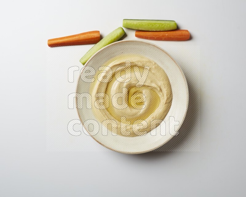 Hummus in a pottry plate garnished with olive oil on a white background
