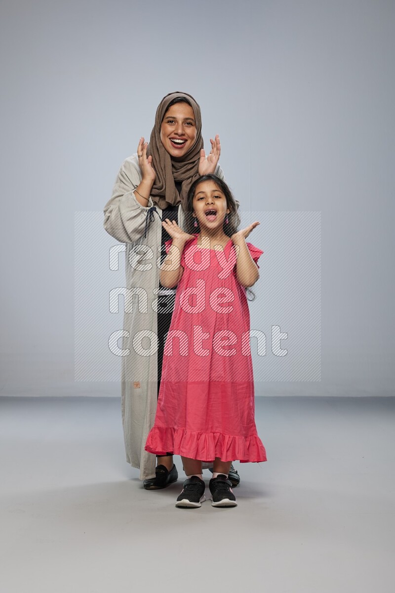 A girl and her mother interacting with the camera on gray background