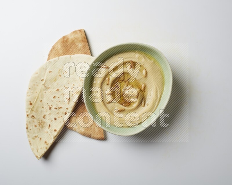 Hummus in a green plate garnished with pine nuts on a white background