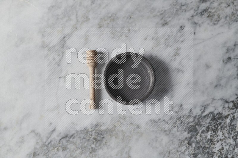 Black pottery bowl with wooden honey dipper on the side on grey marble background