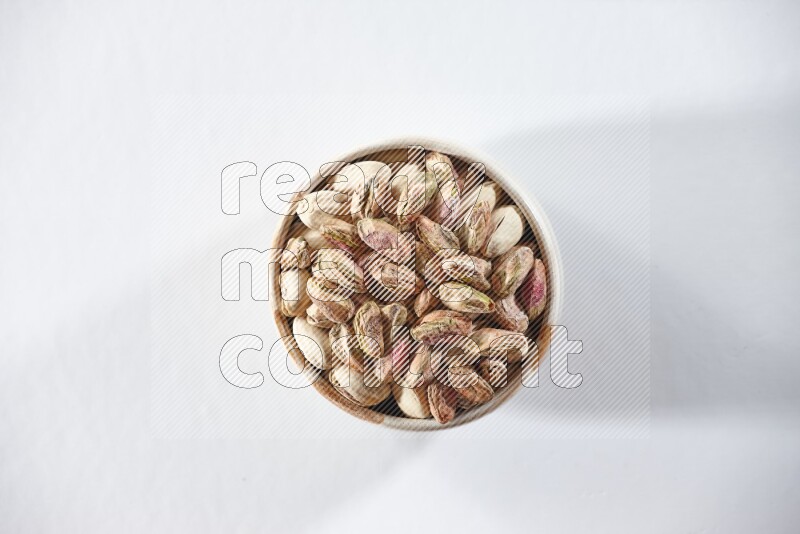 A beige ceramic bowl full of peeled pistachios on a white background in different angles