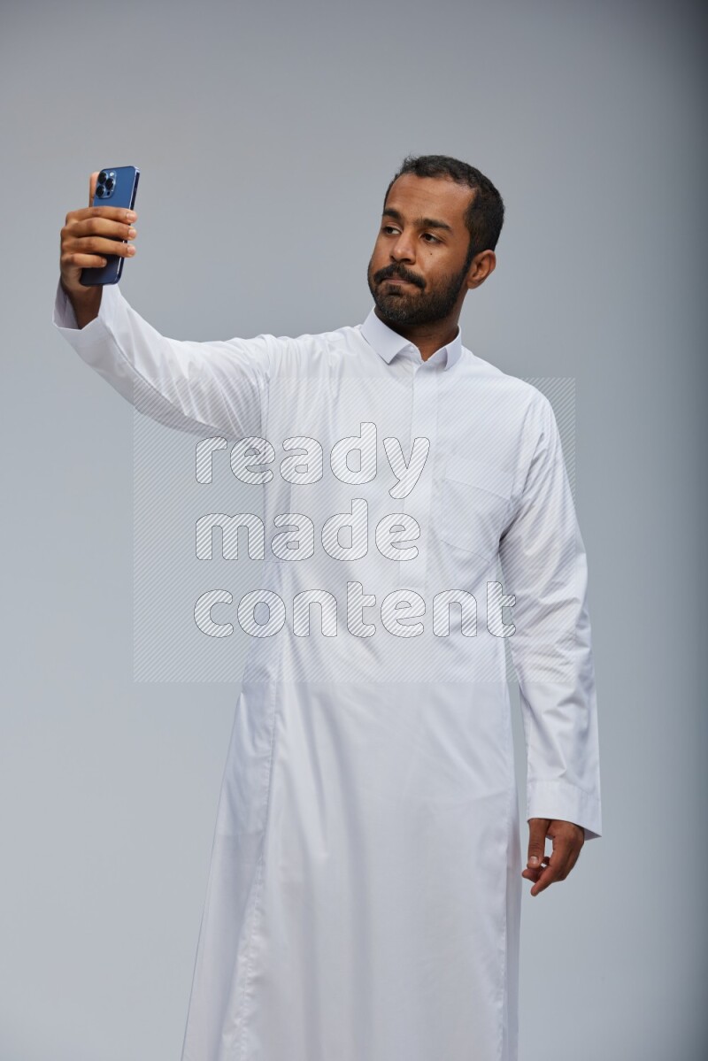 Saudi man wearing Thob standing taking selfie on Gray background