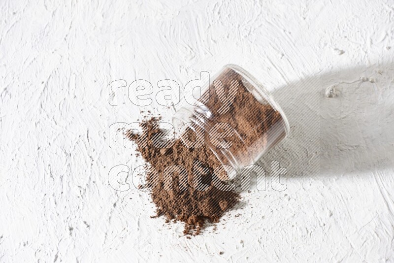 A flipped glass jar full of cloves powder on a textured white flooring