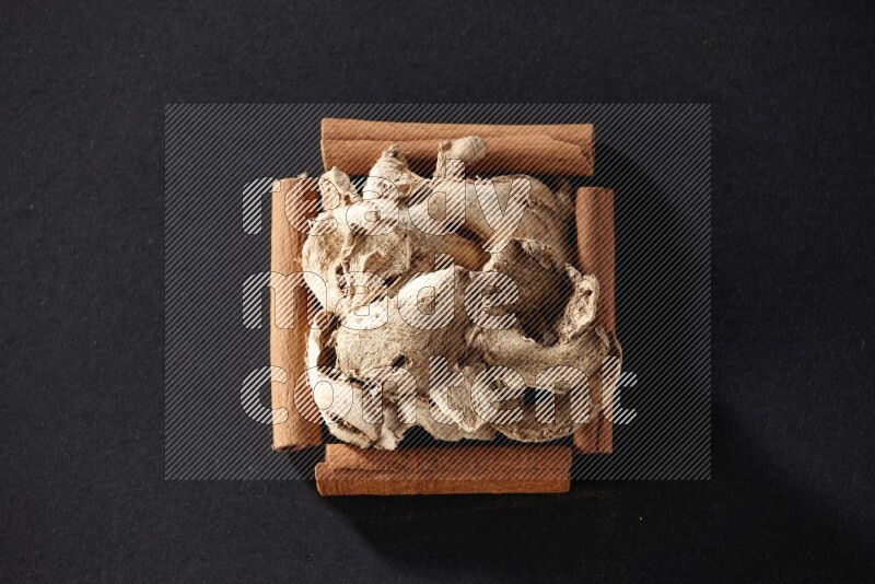 أربعة من أعواد القرفة مكونة شكل مربع بداخلها زنجبيل مجفف علي خلفية سوداء