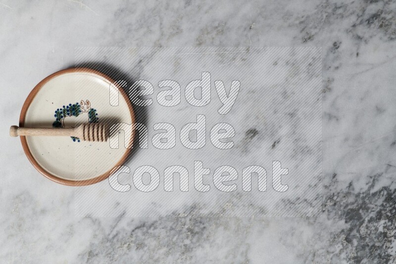 طبق فخاري مزخرف مع ملعقة عسل خشبية بداخله على خلفية من الرخام الرمادي