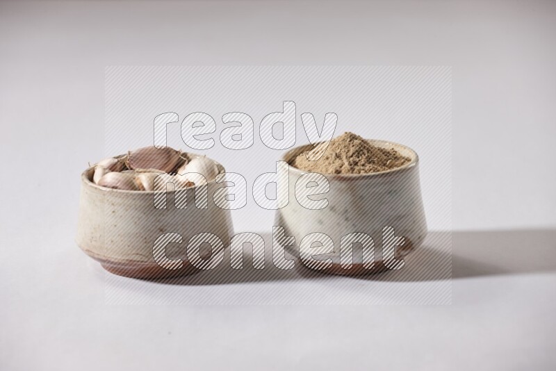 2 beige pottery bowls, one full of garlic powder and the other full of garlic cloves on a white flooring