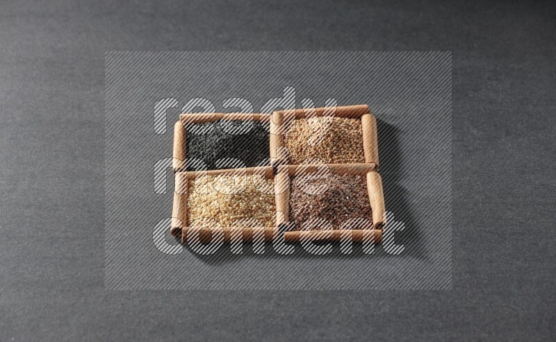 4 squares of cinnamon sticks full of black seeds, sesame, flaxseeds and mustard seeds on black flooring
