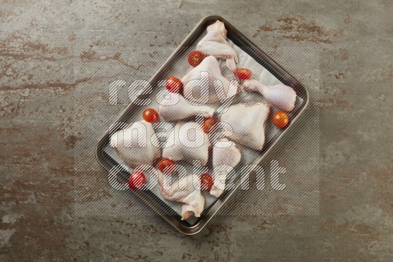 Mixed fresh chicken pieces in an oven tray on a textured rustic background