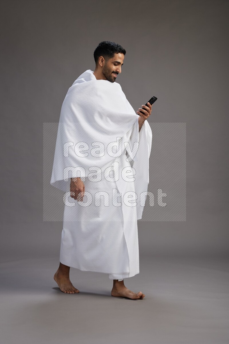 A man wearing Ehram Standing texting on phone on gray background