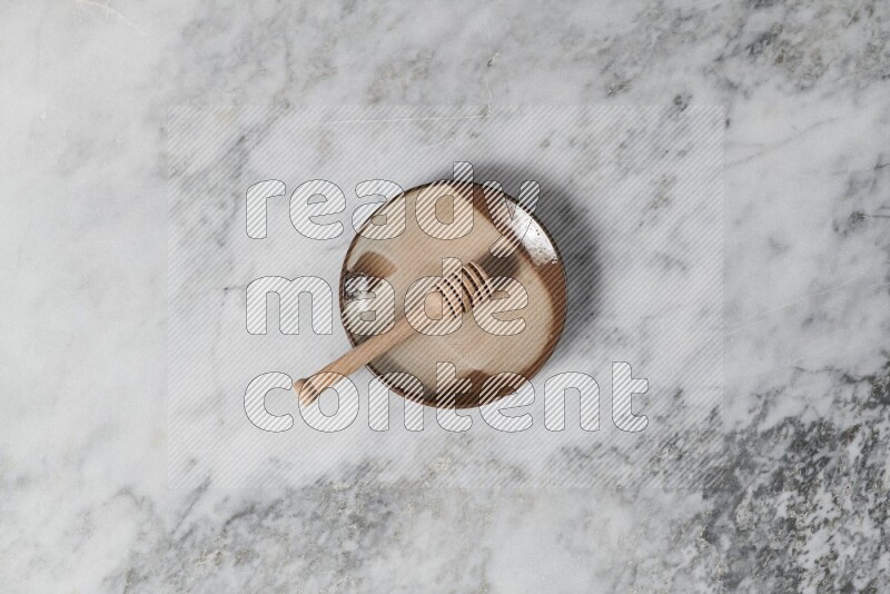 Multicolored pottery plate with wooden honey dipper in it on grey marble background