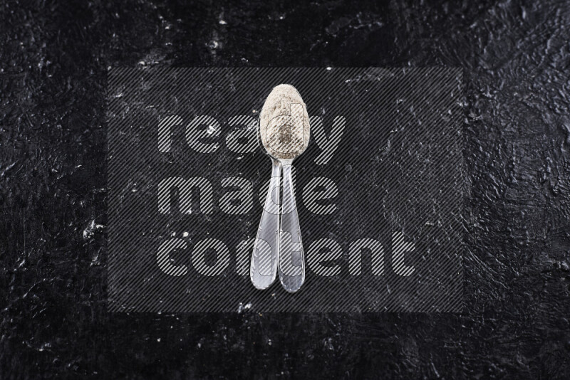 Two metal spoons full of onion powder on black background