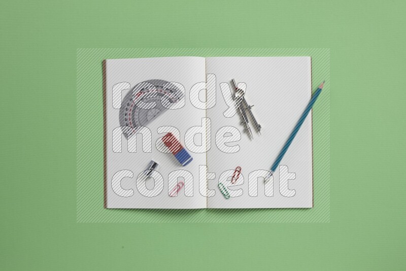 A blank open notebook with different school supplies on green background