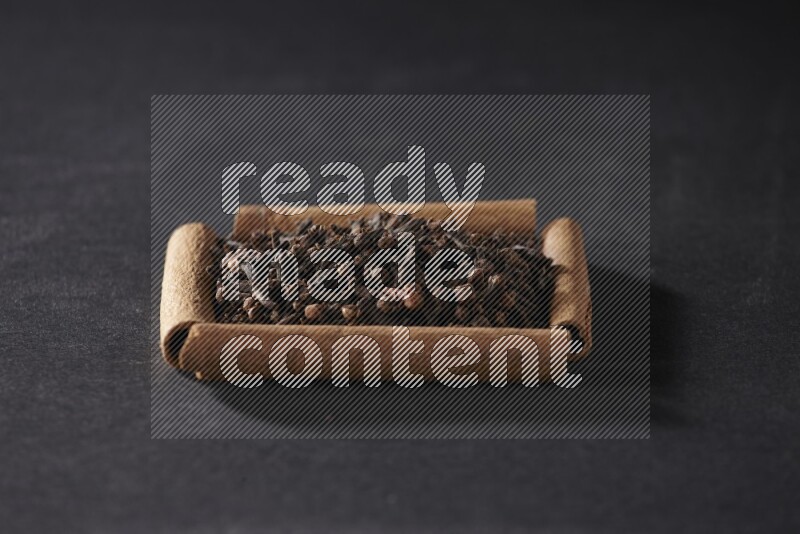 A single square of cinnamon sticks full of cloves on black flooring