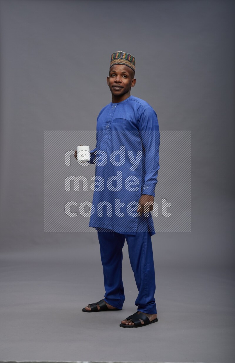 Man wearing Nigerian outfit standing holding mug on gray background