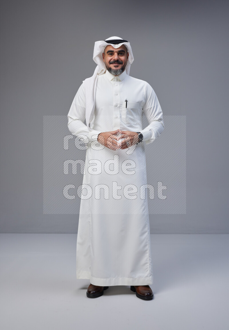 Saudi man Wearing Thob and white Shomag standing interacting with the camera on Gray background