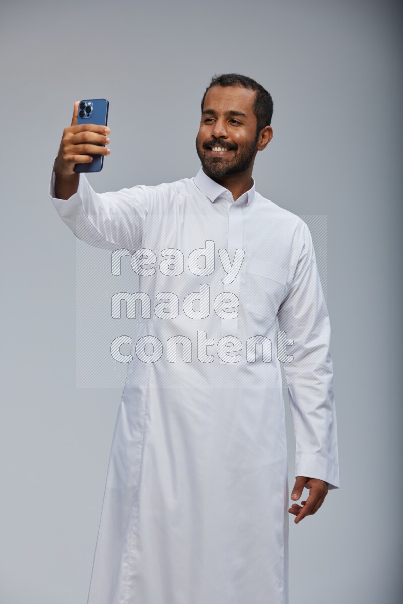 Saudi man wearing Thob standing taking selfie on Gray background