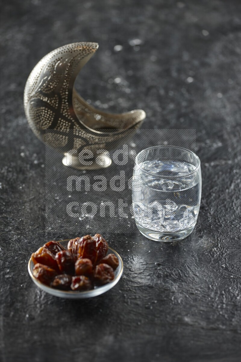 A silver lantern with different drinks, dates, nuts, prayer beads and quran on textured black background