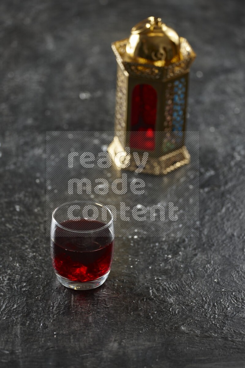 A golden lantern with different drinks, dates, nuts, prayer beads and quran on textured black background