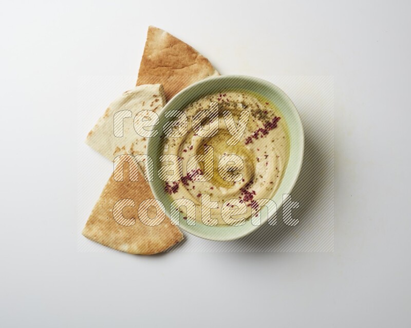 Hummus in a green plate garnished with zattar & sumak on a white background